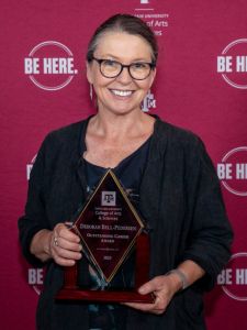 Deb Bell-Pedersen holding award in front of maroon background