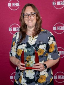 Angela Mitchell holding award in front of maroon background