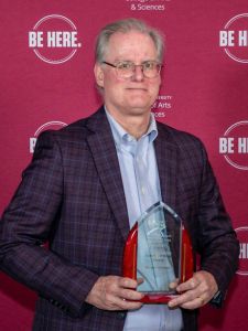 picture of Wayne Versaw holding an award in front of a maroon background